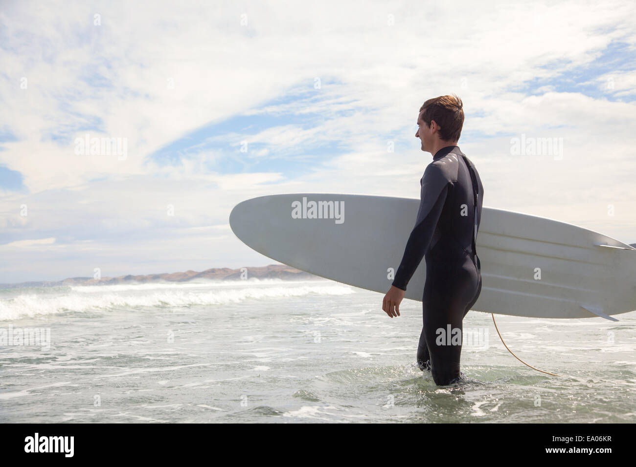 Young man carrying surfboard, walking out to sea Stock Photo