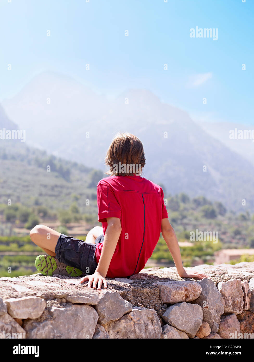 Boy sitting on stone wall gazing at view, Majorca, Spain Stock Photo