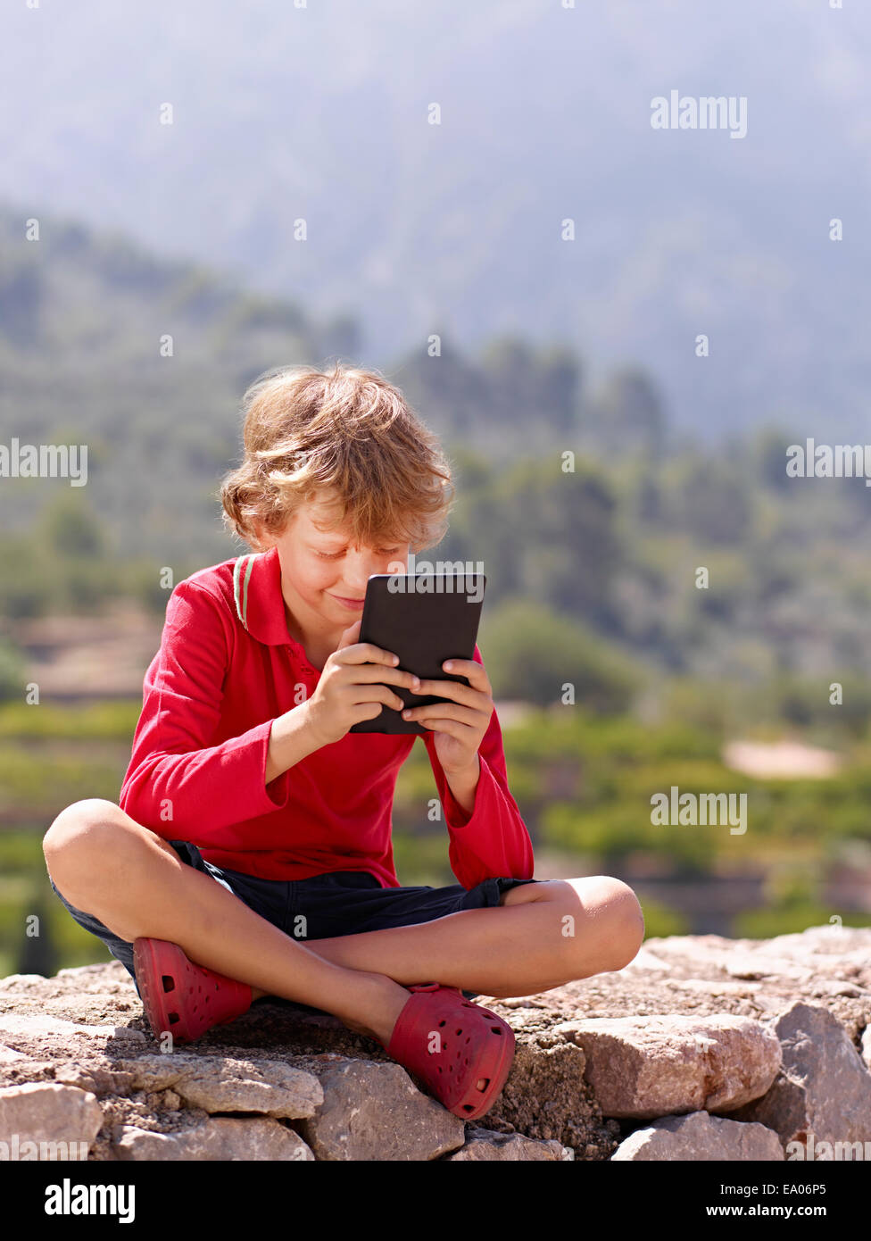 Boy sitting on stone wall looking at digital tablet, Majorca, Spain Stock Photo