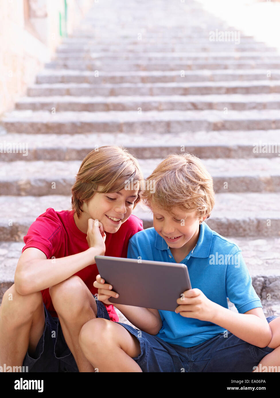 Brothers looking at digital tablet on village steps, Majorca, Spain Stock Photo