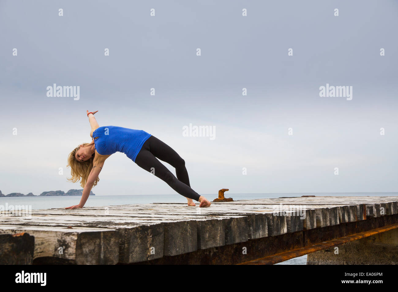 Mid adult woman practicing yoga move on wooden sea pier Stock Photo