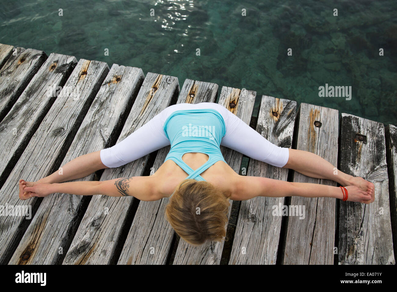 Overhead view of mid adult woman with arms and legs outstretched practicing yoga on wooden sea pier Stock Photo