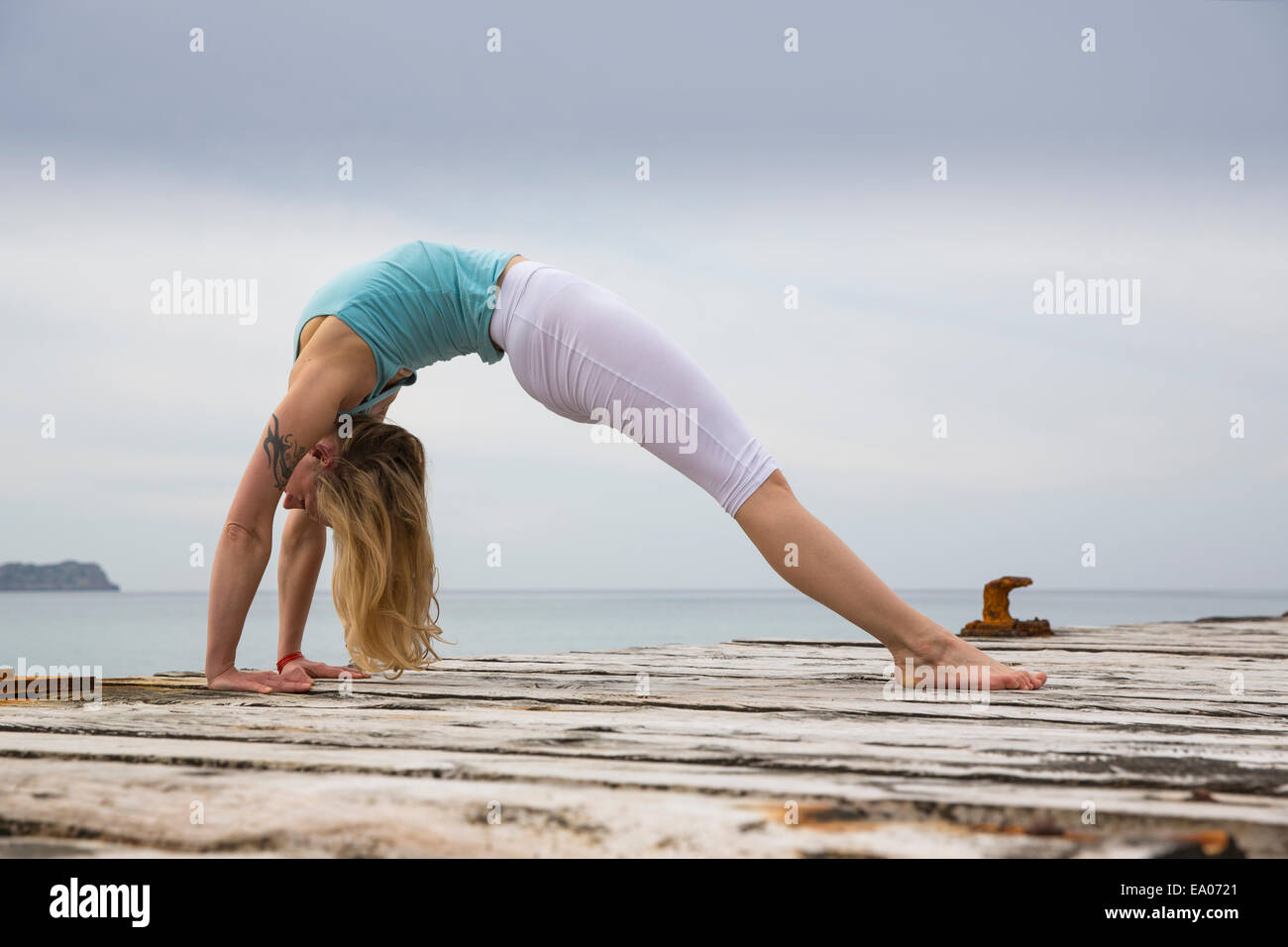 Mid adult woman bending over backwards practicing yoga on wooden sea pier Stock Photo