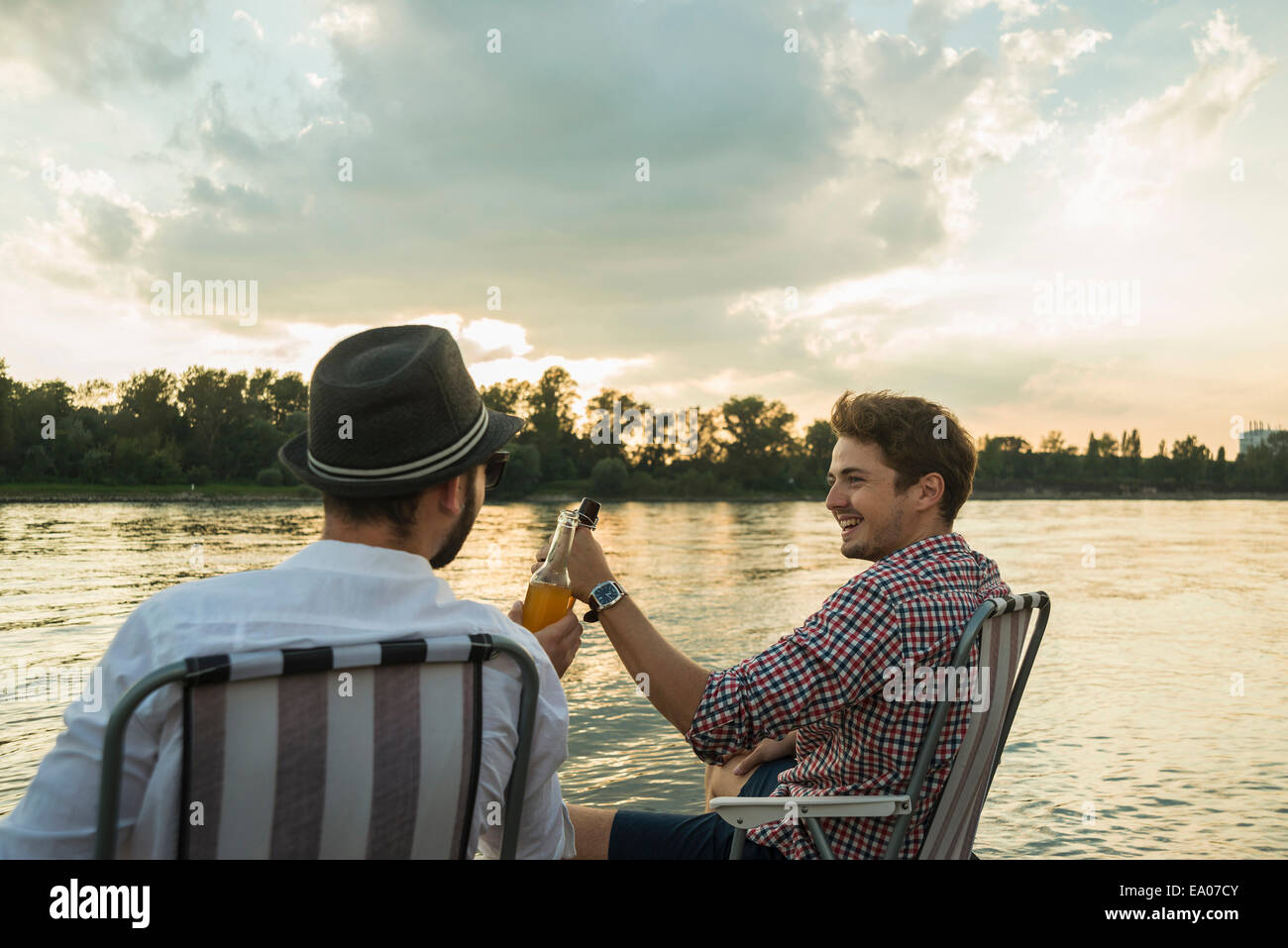 Young men toasting with beer bottles by lake Stock Photo