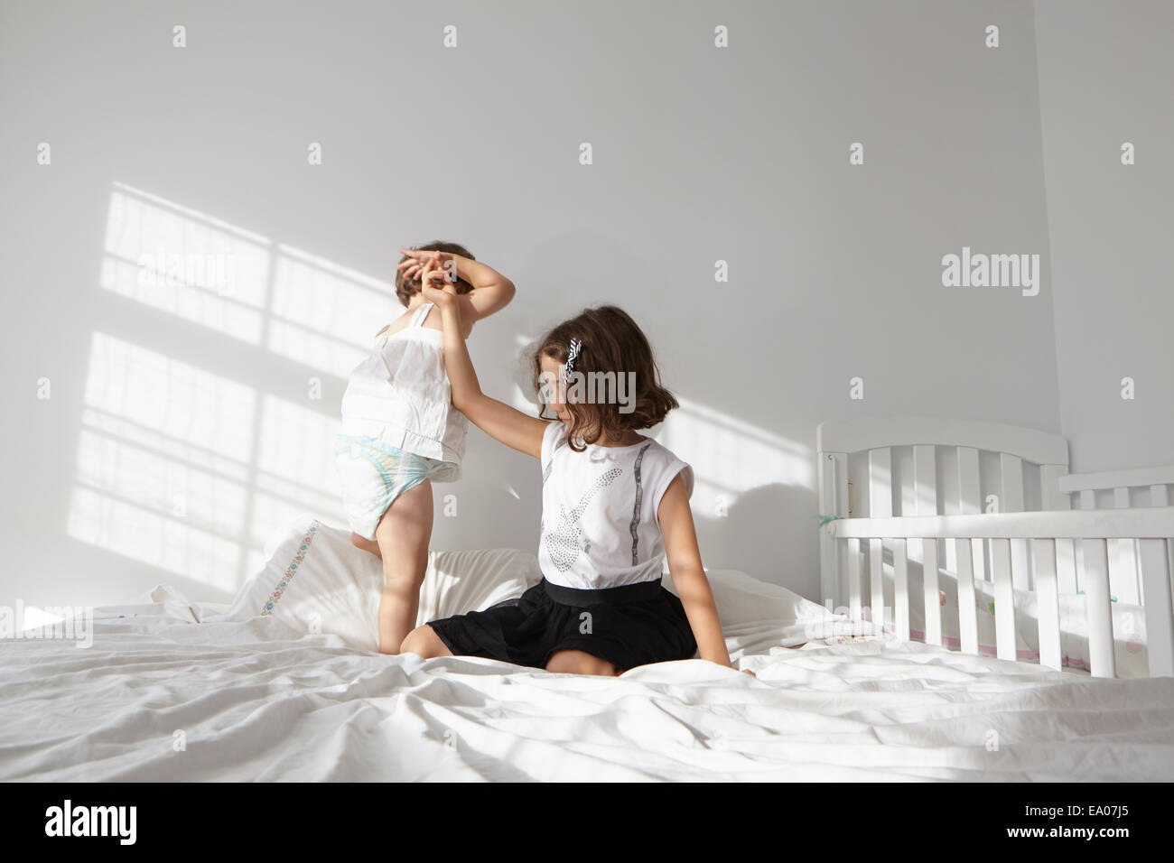 Girl giving helping hand to female toddler cousin to toddle on bed Stock Photo