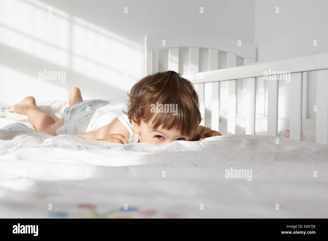 Candid portrait of female toddler peeking over bed quilt Stock Photo