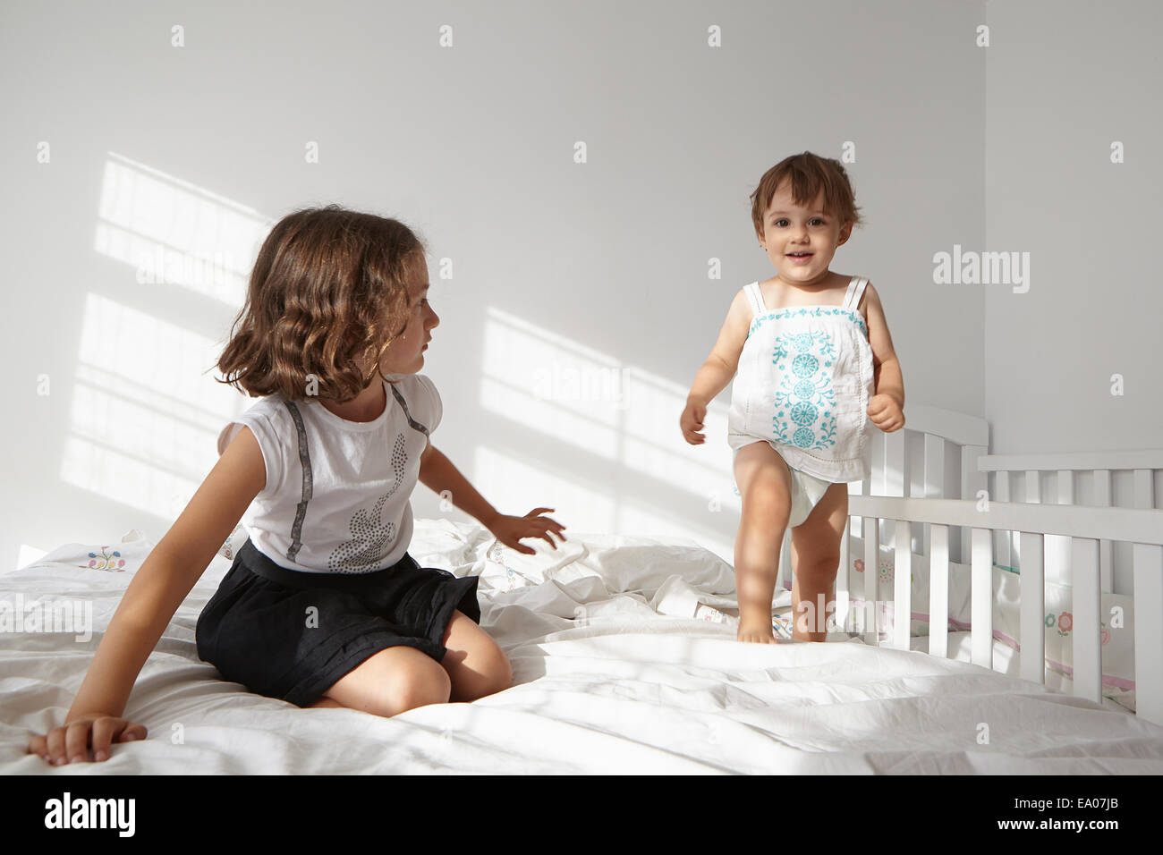 Girl watching female toddler cousin to toddle on bed Stock Photo