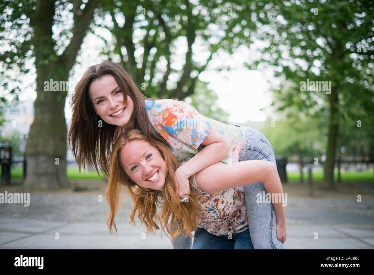 Portrait of two young female best friends giving piggy back in park Stock Photo