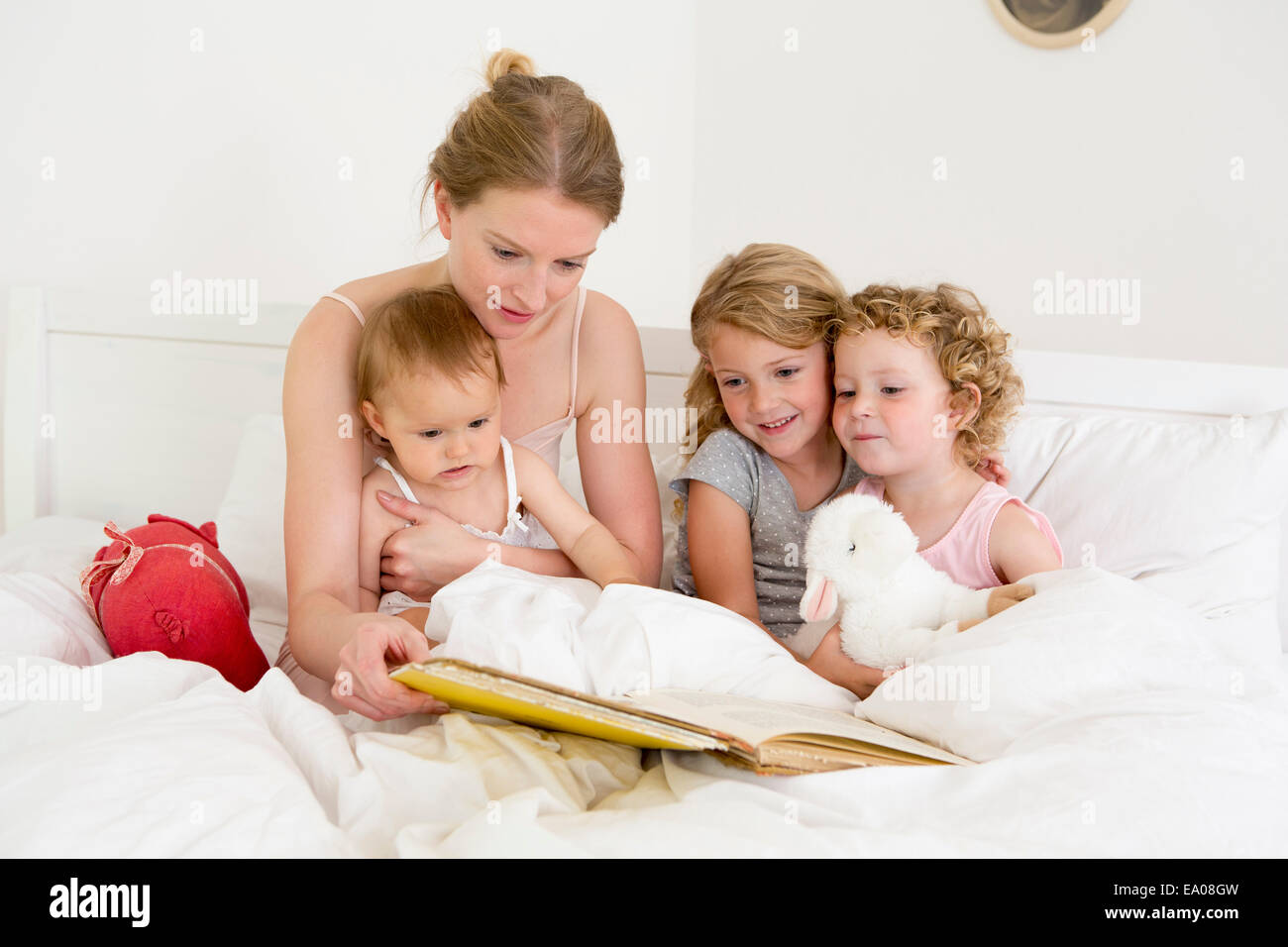 Mother reading book to three daughters in bed Stock Photo