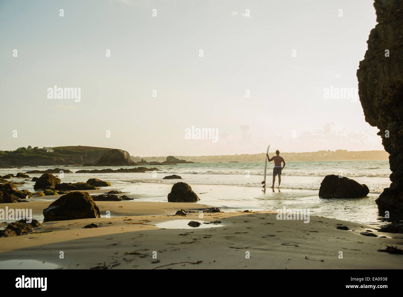 Mature man standing at waters edge holding surf board Stock Photo