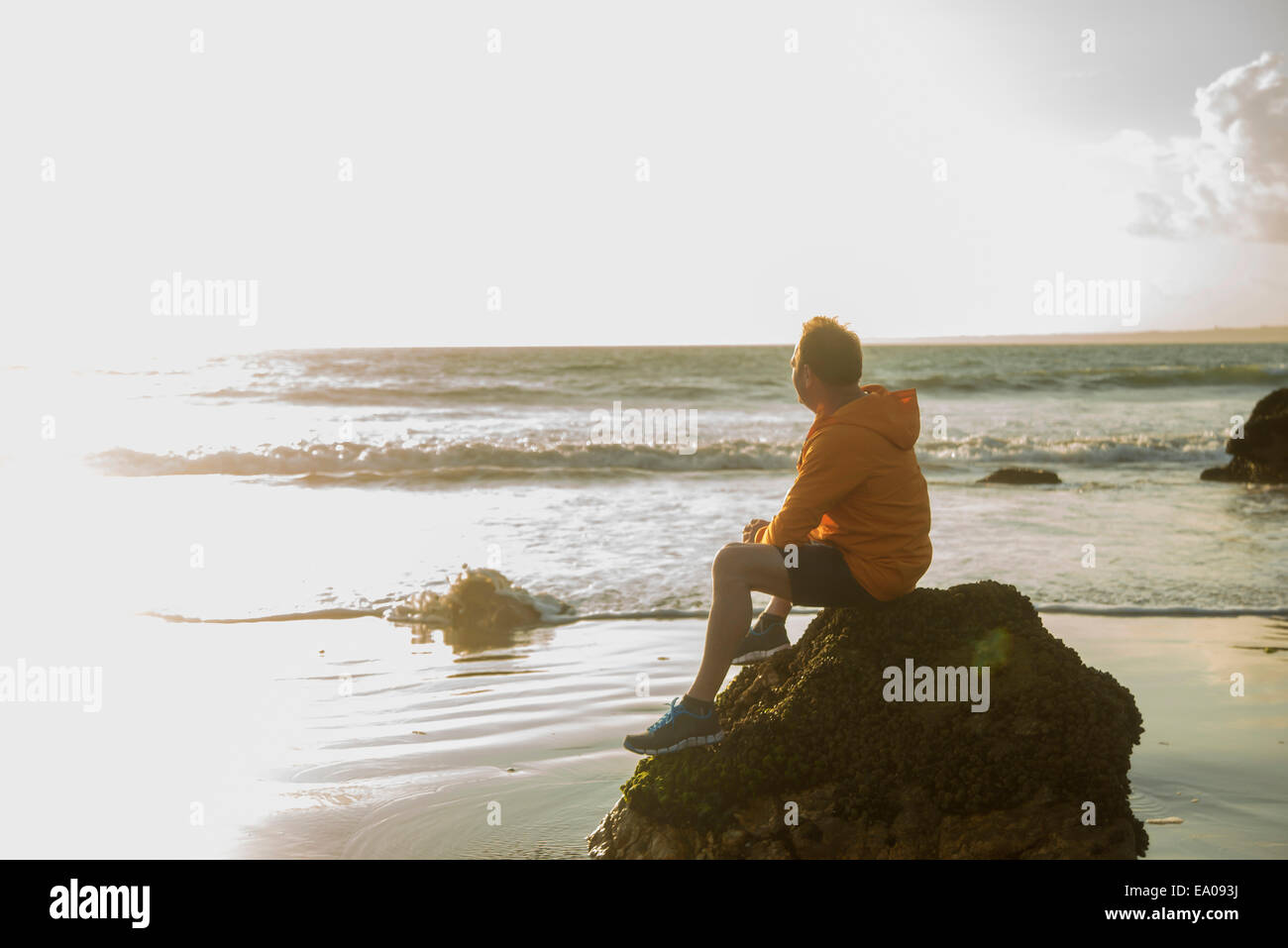 Mature man, sitting on rock, looking out to sea Stock Photo