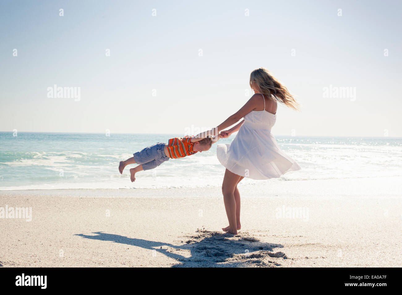 Mid Adult Mother Swinging Young Son By Hands On Beach Cape