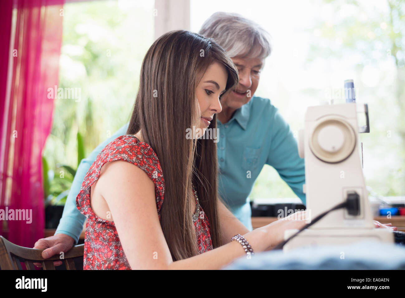 Senior woman watching granddaughter use sewing machine Stock Photo