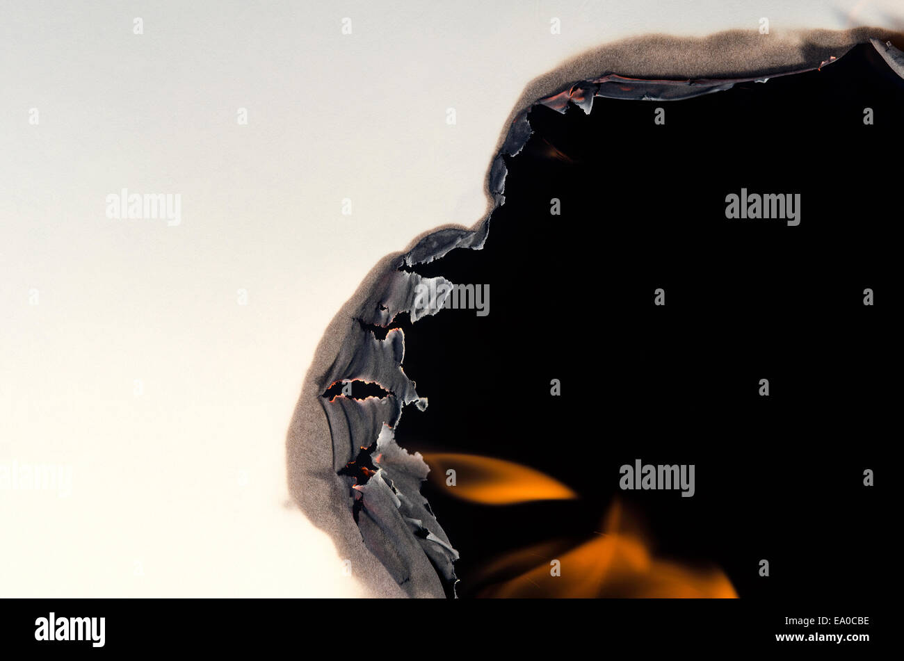 A burning hole forms on the side of a white sheet of paper Stock Photo