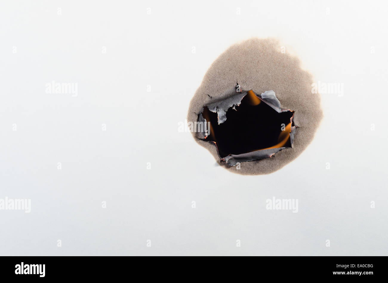 A hole burns through a white sheet of paper with black behind Stock Photo