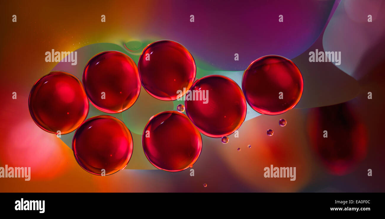 macro of red engine oil drops on water surface with colorful blured background Stock Photo