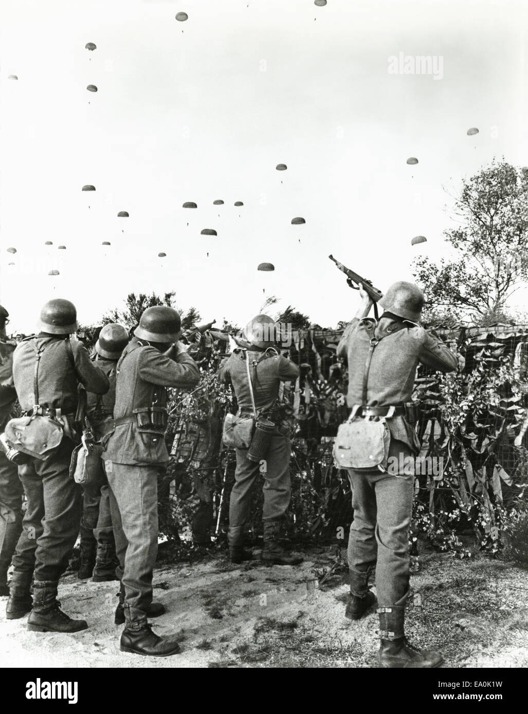 Soldiers shooting at enemy parachuting into field Stock Photo