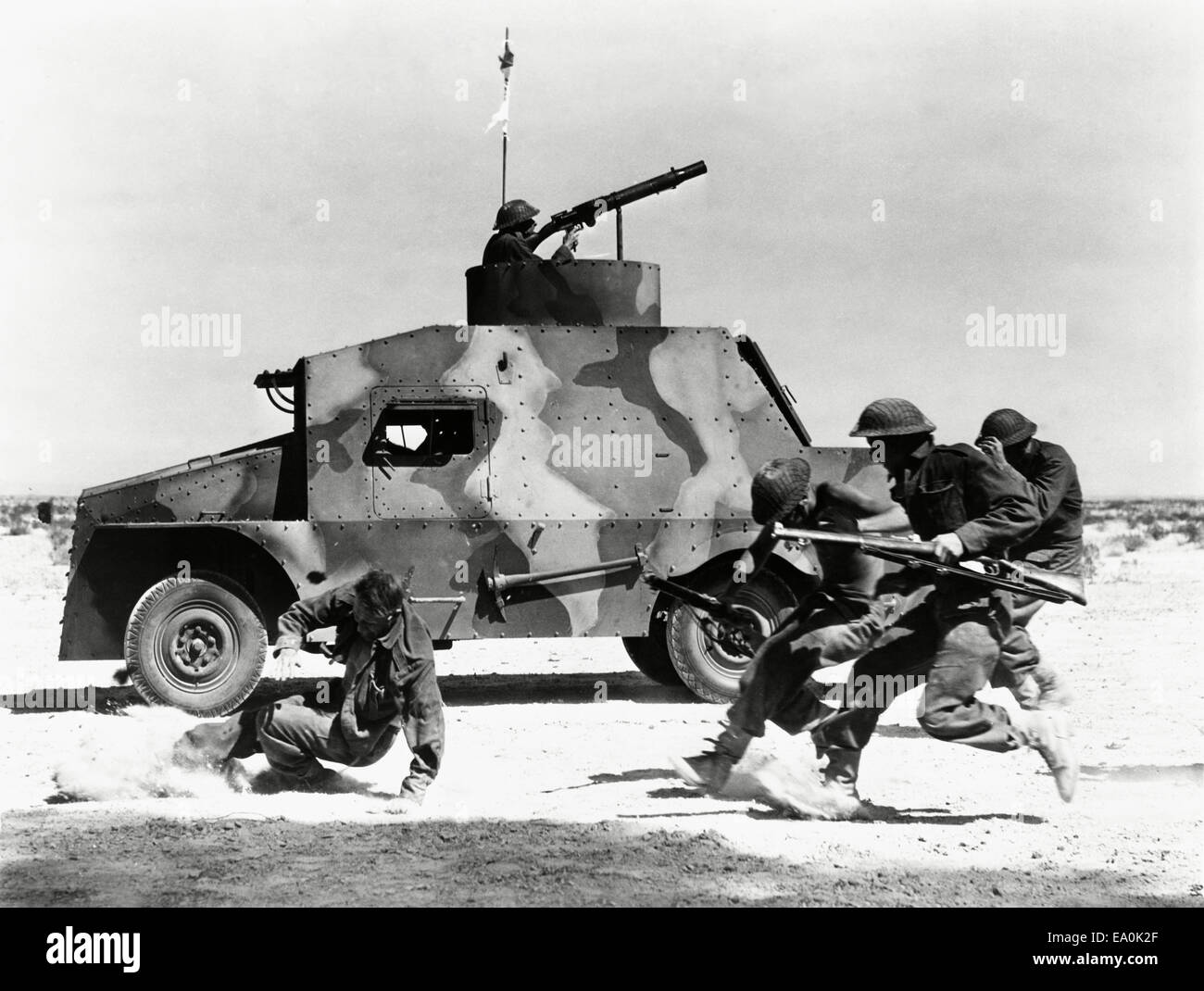 Soldiers running along side of tank in the desert Stock Photo