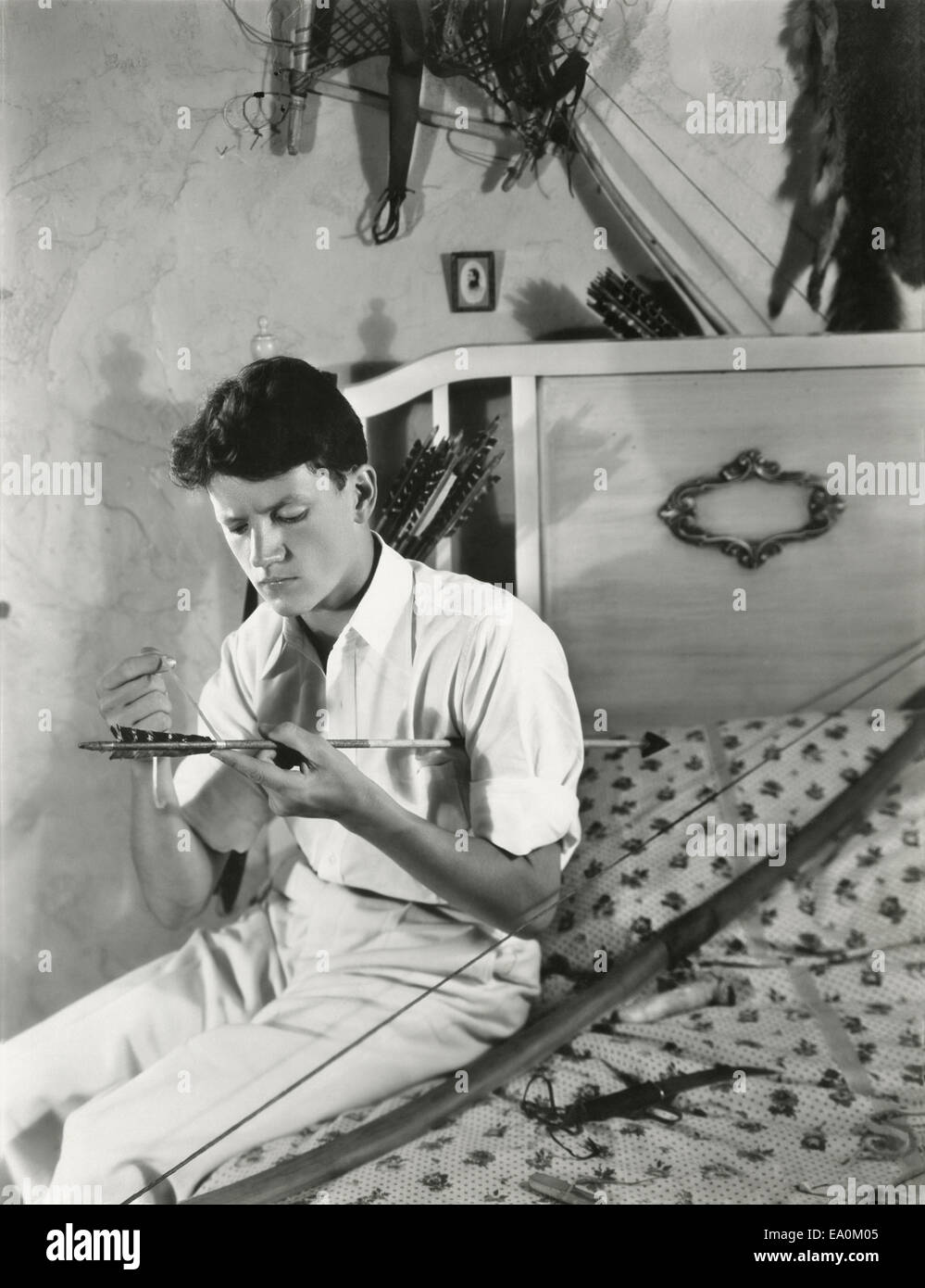 A young man mends his bow and arrow Stock Photo