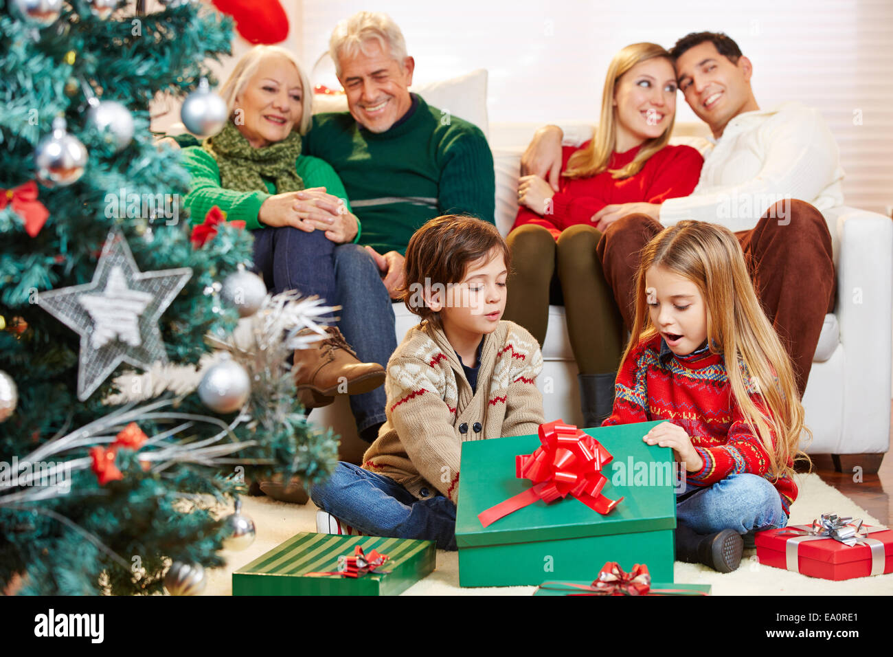 Happy children opening gifts at christmas while parents and grandparents are watching Stock Photo