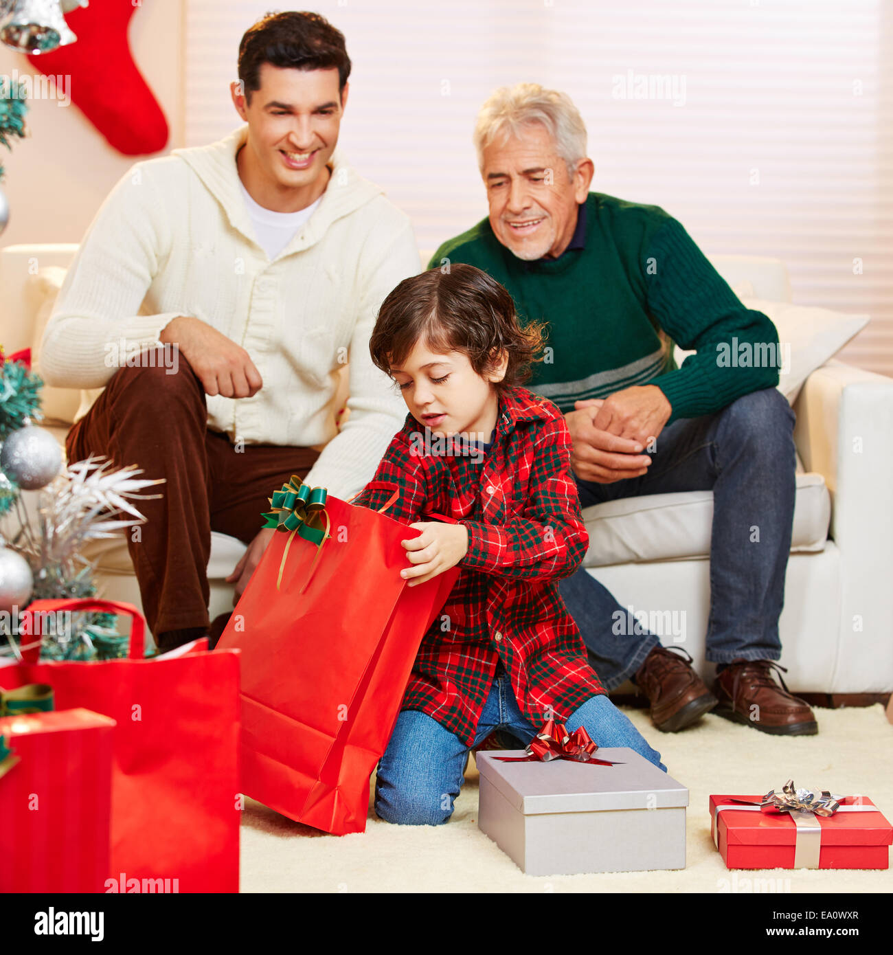 Happy boy opening gifts at christmas and father and grandfather watching Stock Photo