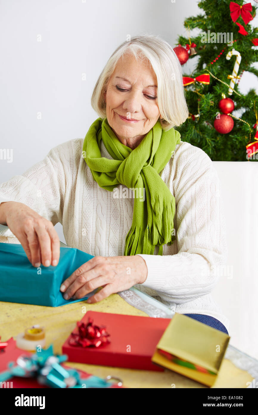 Senior woman wrapping gifts for christmas with wrapping paper Stock