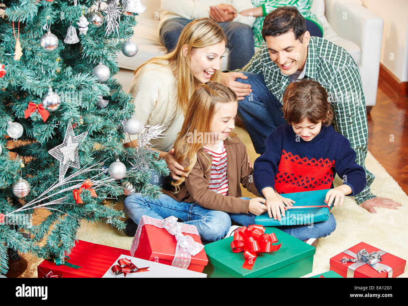Children opening gifts at christmas eve while the family is watching Stock Photo