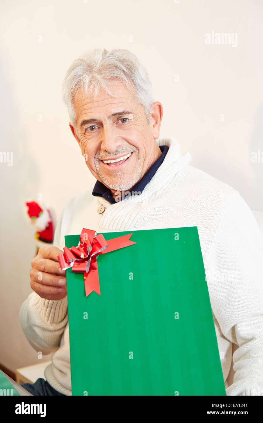 Senior man holding green gift with red ribbon at christmas Stock Photo