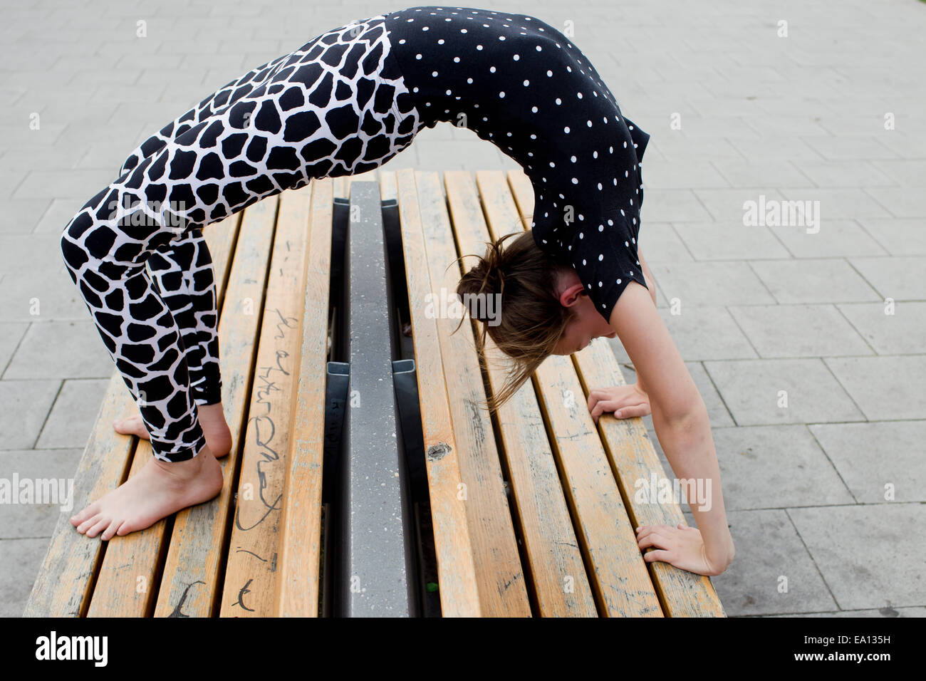 Teenage girl doing backwards bend on bench Stock Photo