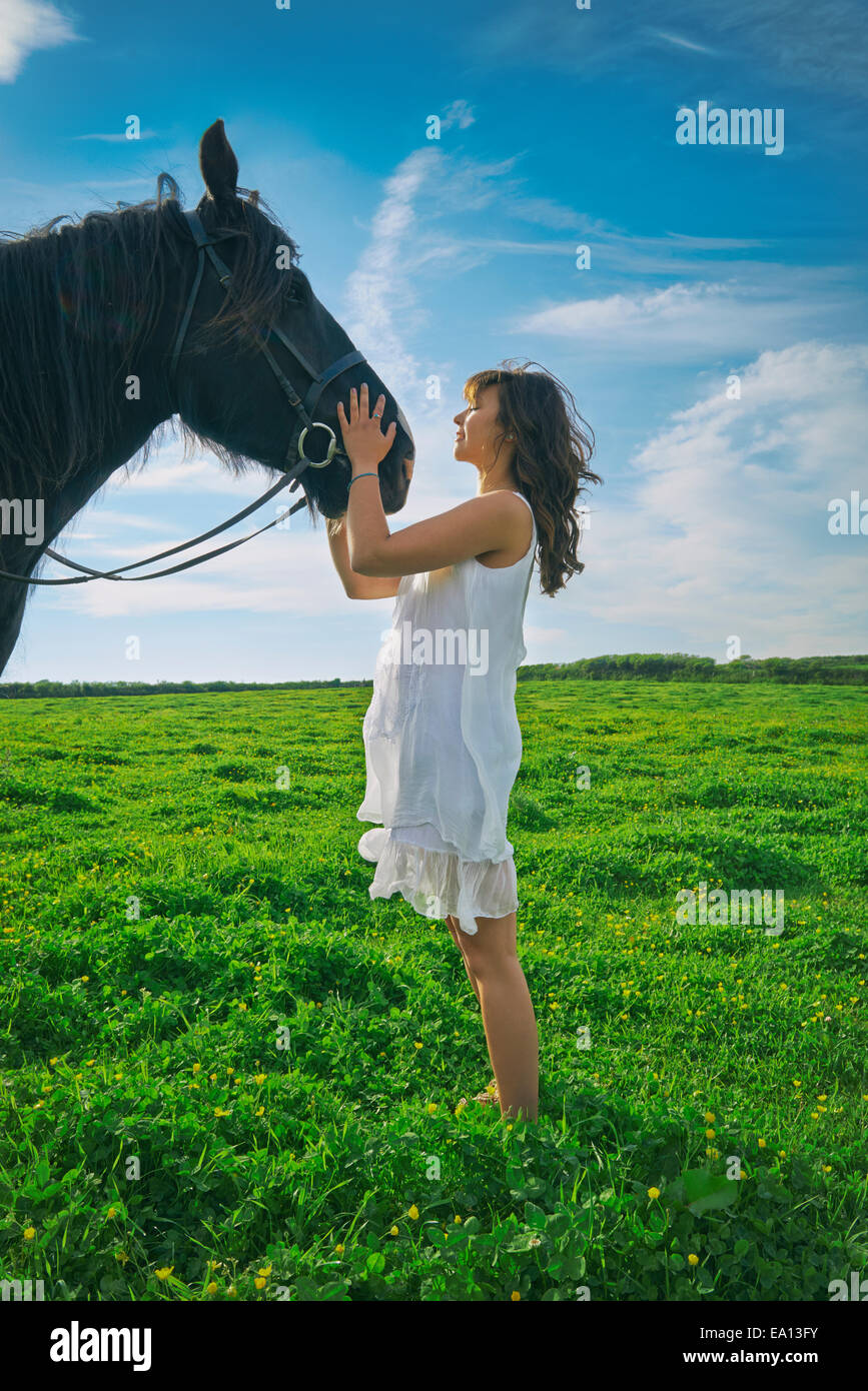 Young woman petting horse in field Stock Photo