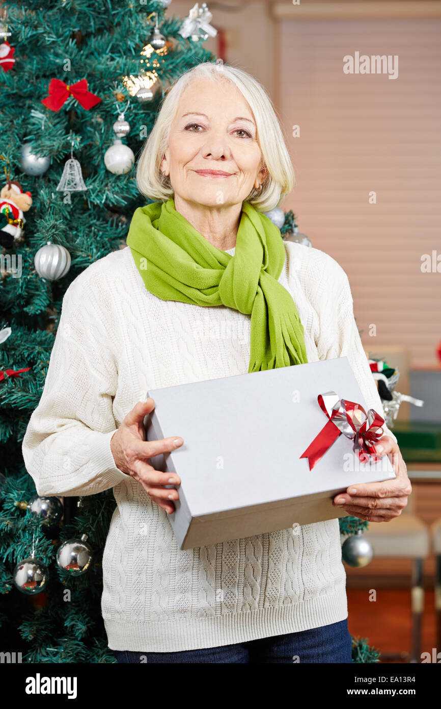 Smiling senior woman on christmas holding a gift in front of christmas tree Stock Photo