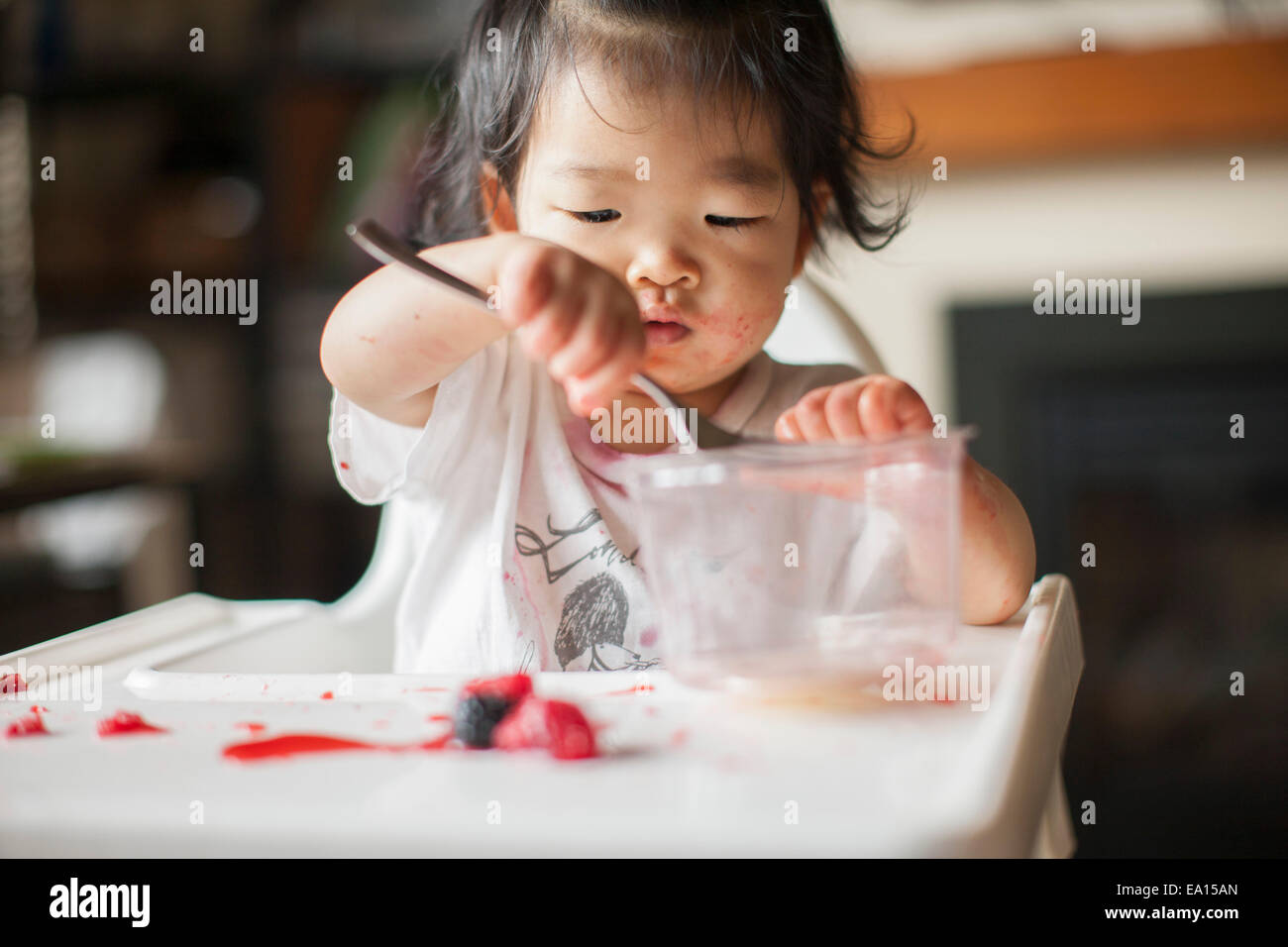 One year old baby girl eating fruit in highchair Stock Photo