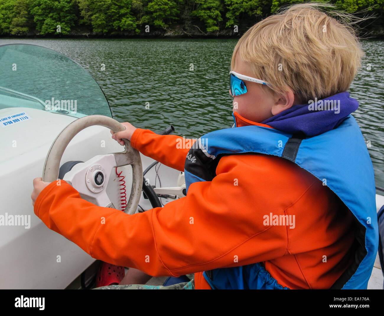 A boy driving a rented motor boat across flat river estuary Stock Photo