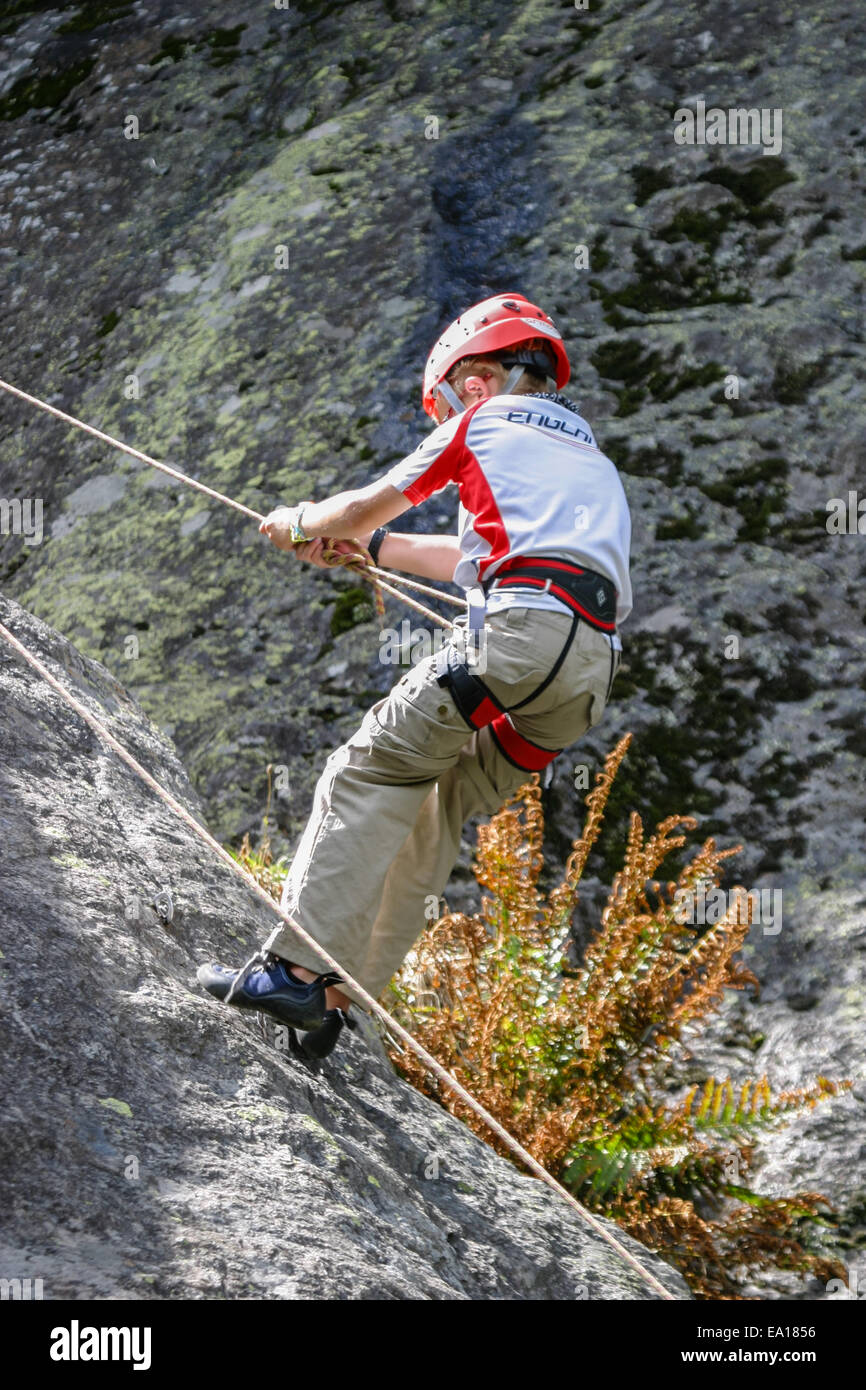 A young boy in full climbing equipment abseiling down a rock face Stock Photo