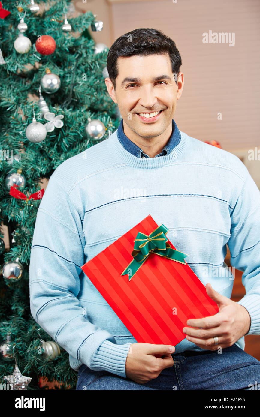 Smiling man holding a red gift at christmas tree Stock Photo
