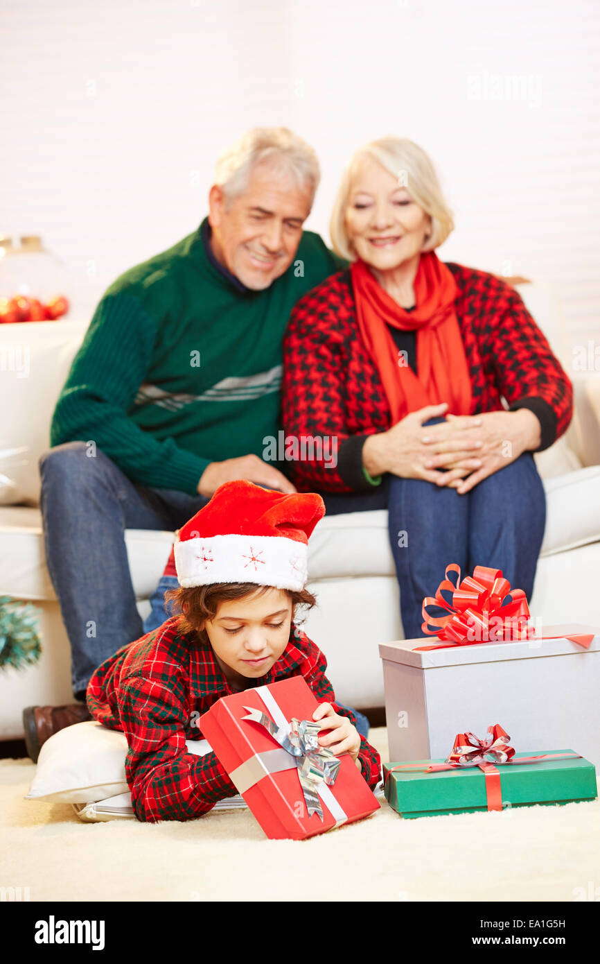 Happy grandparents watching their grandchild opening christmas gifts Stock Photo