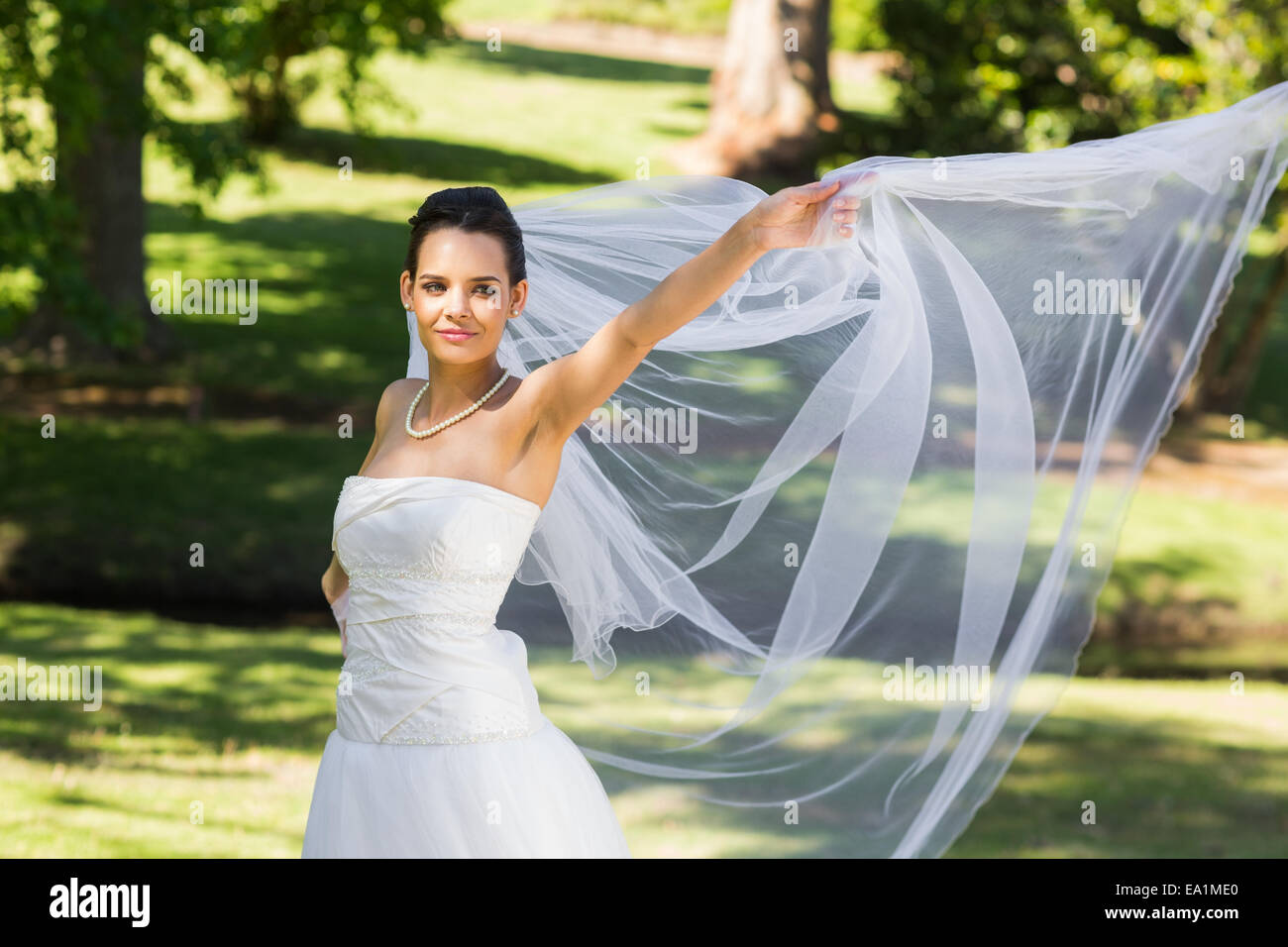 Smiling beautiful bride standing in park Stock Photo - Alamy