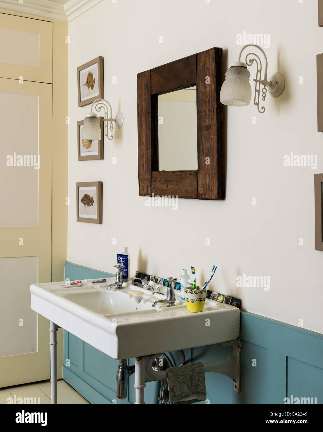 Driftwood style mirror above basin in bathroom with framed fish prints Stock Photo