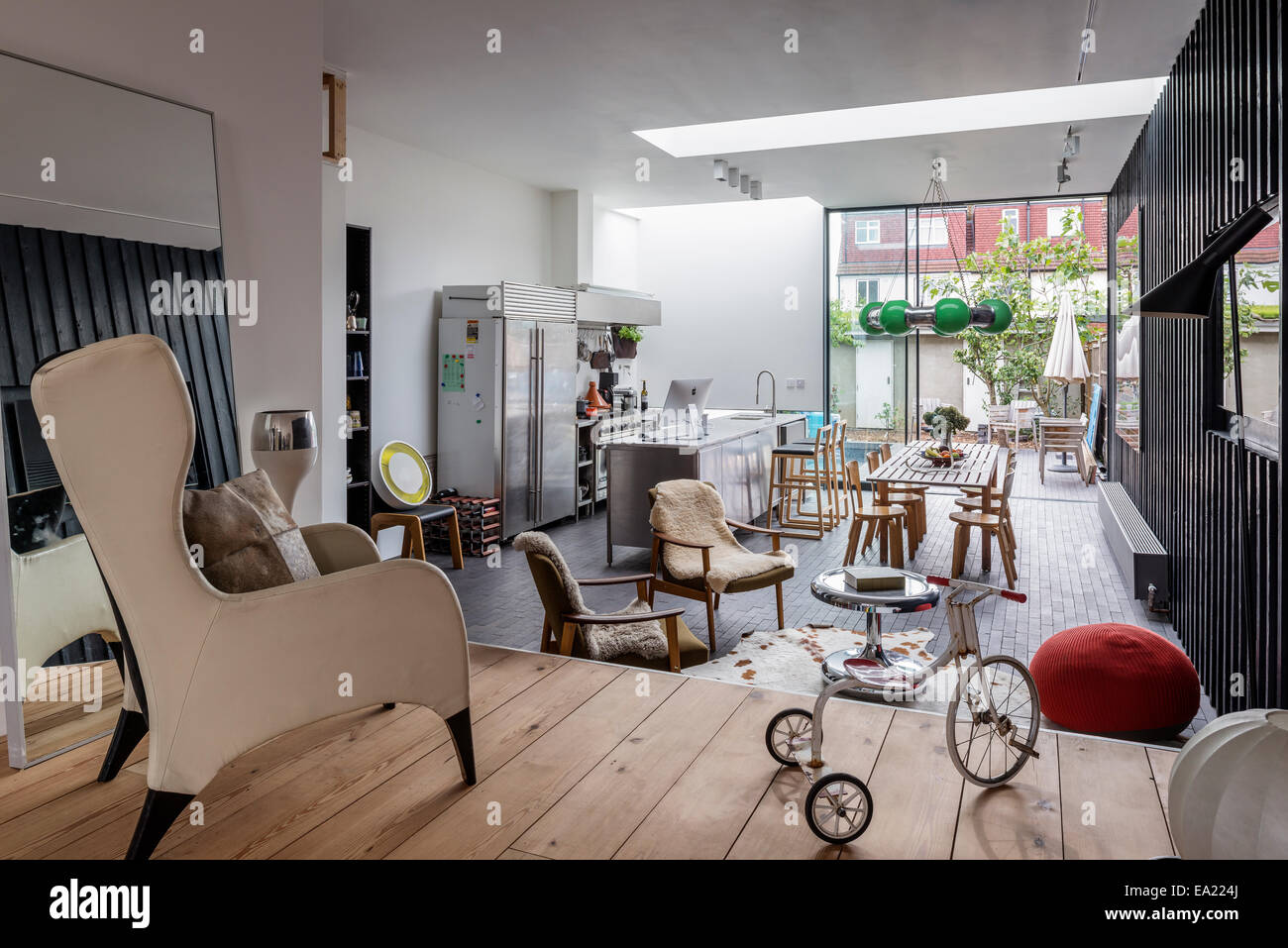 Modern open plan kitchen living space with wingback chair and tricycle in foreground. Stock Photo