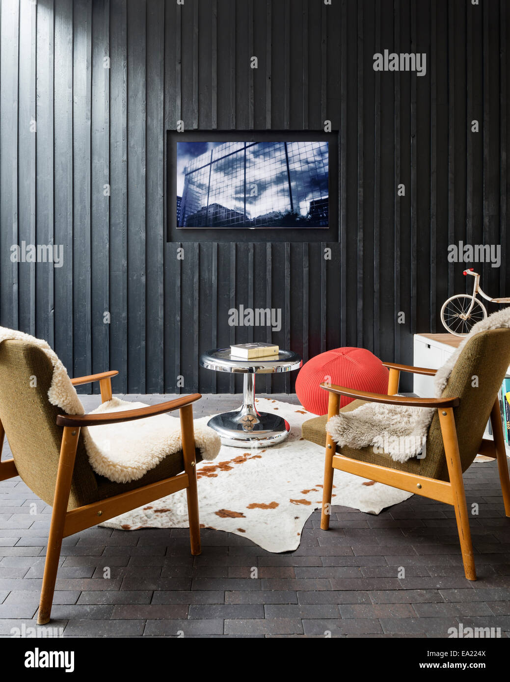 Pair of retro style armchairs with sheepskin in front of a timber clad wall with flatscreen TV Stock Photo