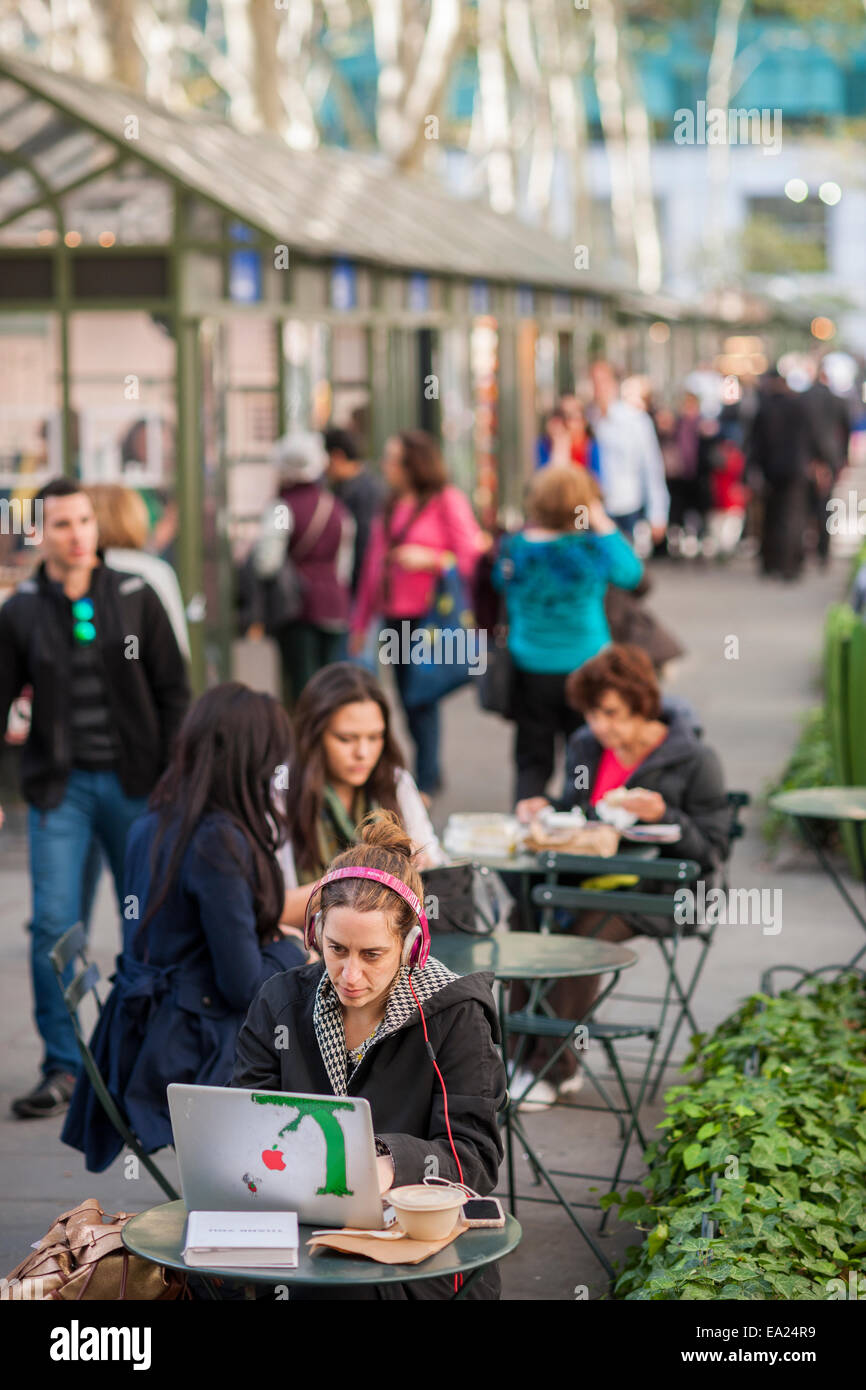 A park visitor takes advantage of both the unseasonable warm weather and the free wi-fi in Bryant Park Stock Photo