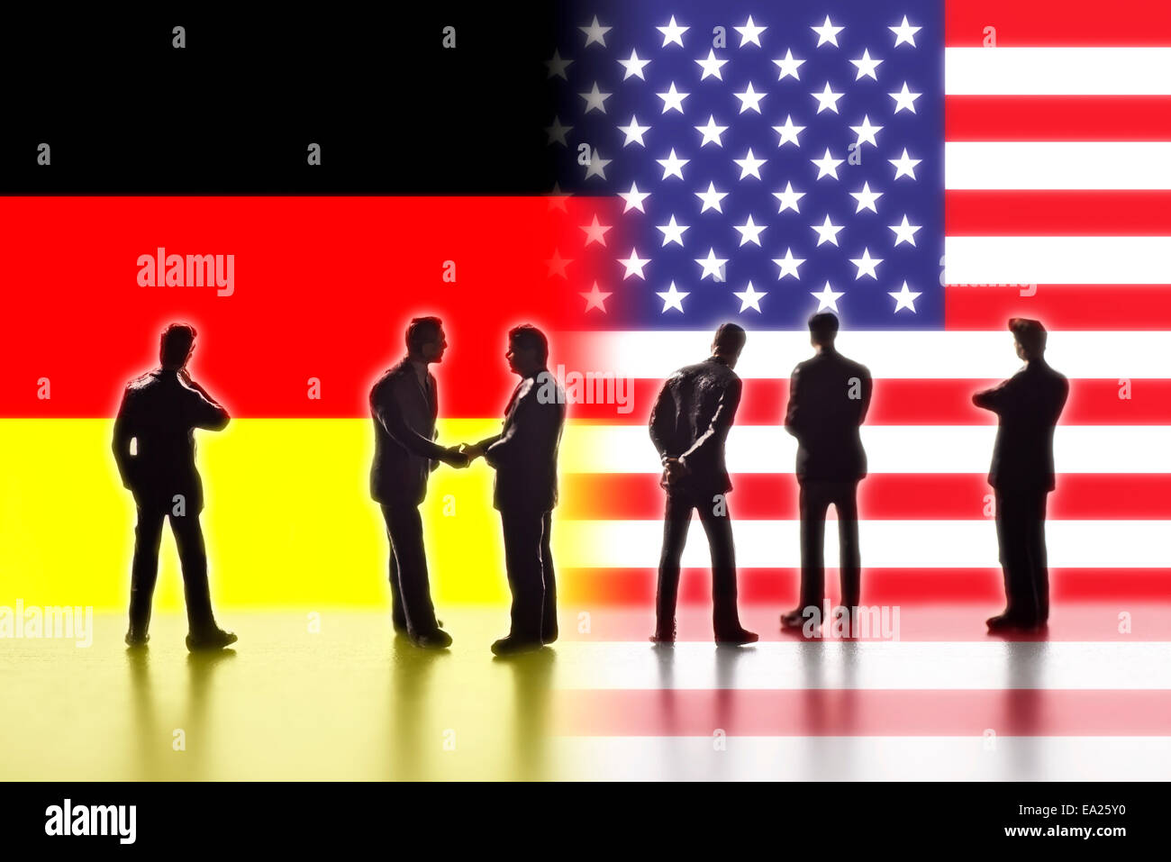 Model figures symbolizing politicians are facing the flags of the USA and Germany. Two of them shake hands. Stock Photo