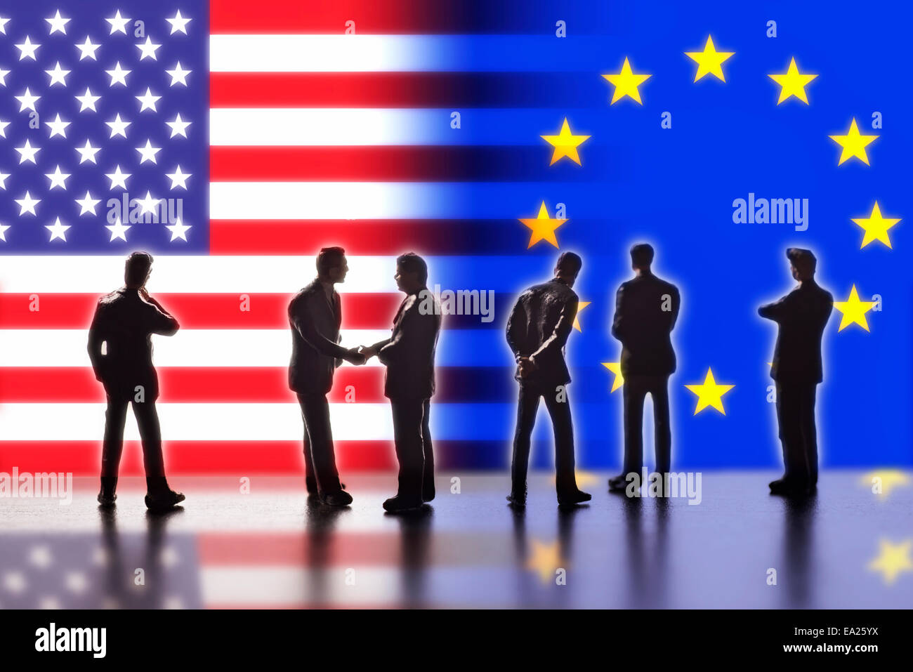 Model figures symbolizing politicians are facing the flags of the USA and the EU. Two of them shake hands. Stock Photo