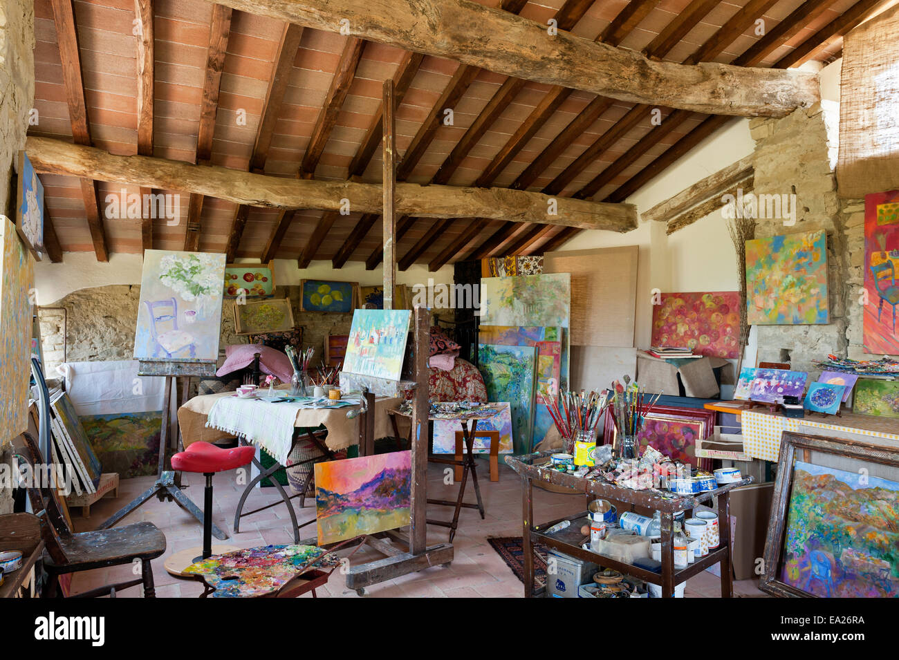Rustic painters studio with brightly coloured artworks, paints and beamed ceiling Stock Photo