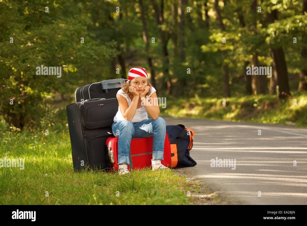 Young hitch-hiker girl standing on road side afternoon with bags Stock Photo