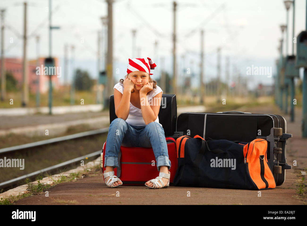Young girl sitting on bag and waiting for train in the station Stock Photo