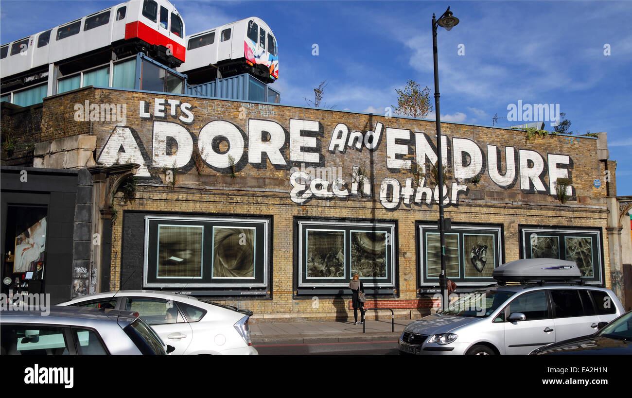 Building in Shoreditch, Easty London adorned with the words,'Lets Adore and Endure Each Other.' Two trains on roof. Stock Photo