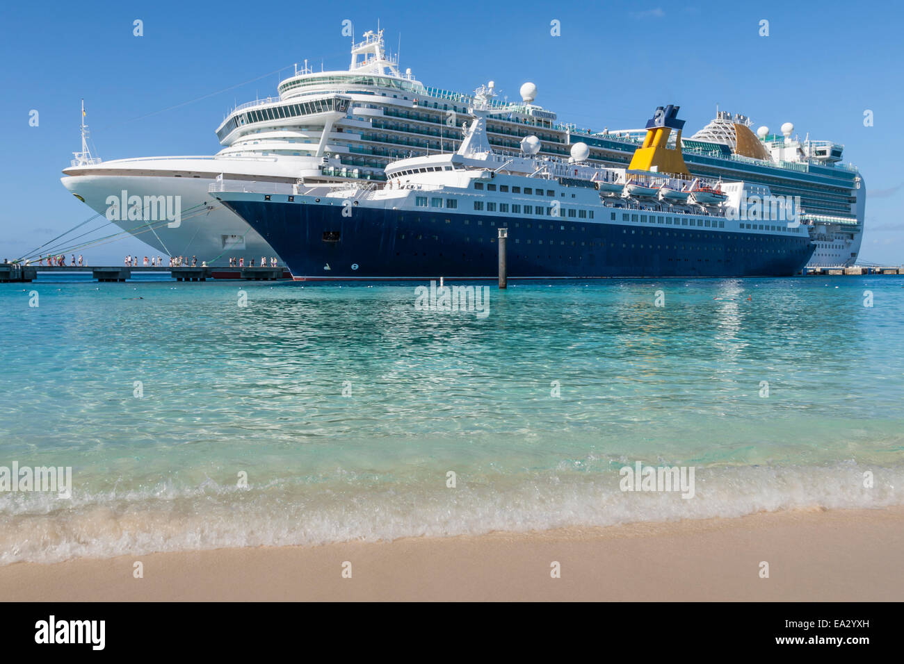 Cruise ships and disembarking passengers, seen from a white sand beach