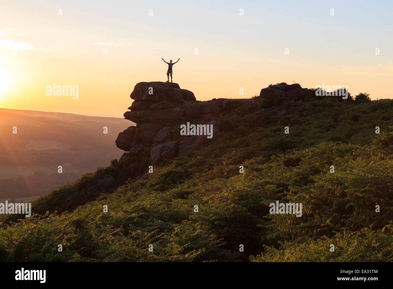 On top of the world, visitor enjoys sunset on Curbar Edge with arms aloft, Peak District National Park, Derbyshire, England, UK Stock Photo