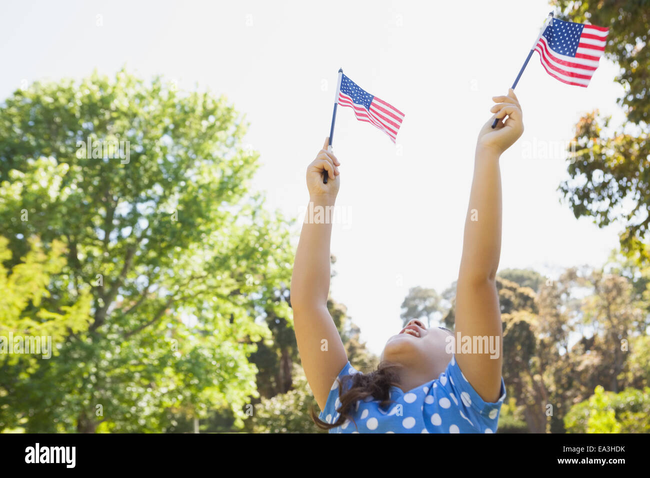 Girl holding up two American flags at park Stock Photo